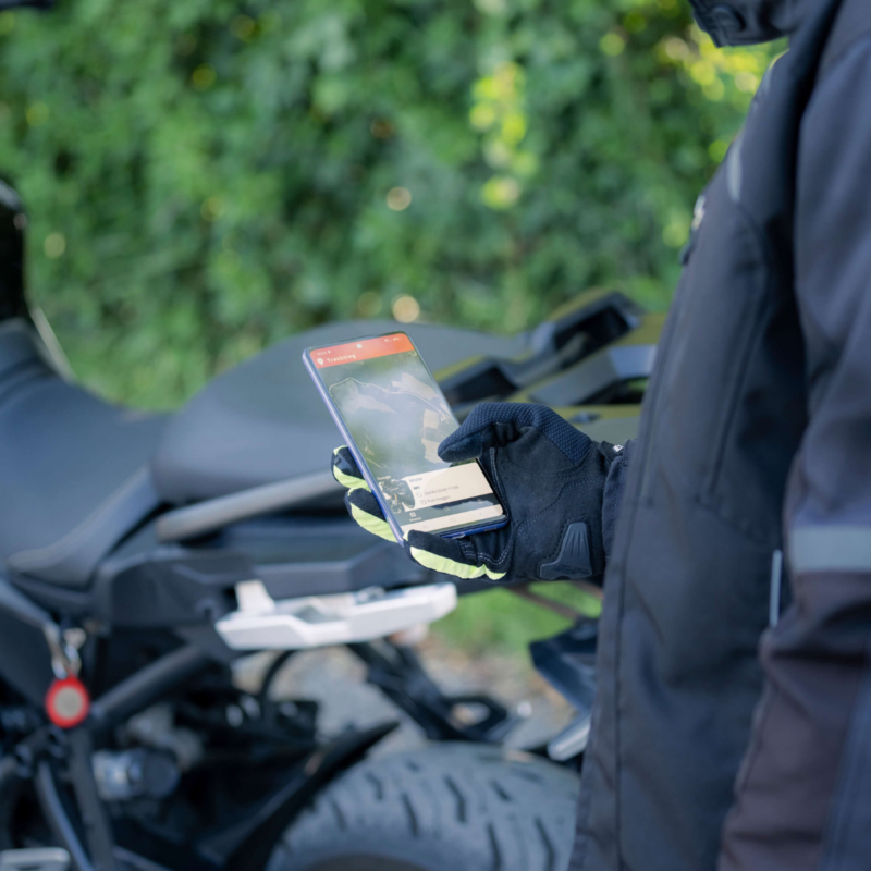 photo about a man looking at Trackting App on his smartphone in front of his motorbike protected by the Antitheft GPS device Trackting